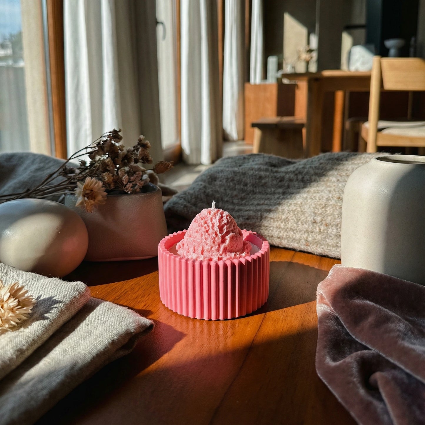 Pink candle in a ribbed container on a wooden surface with a cozy room background