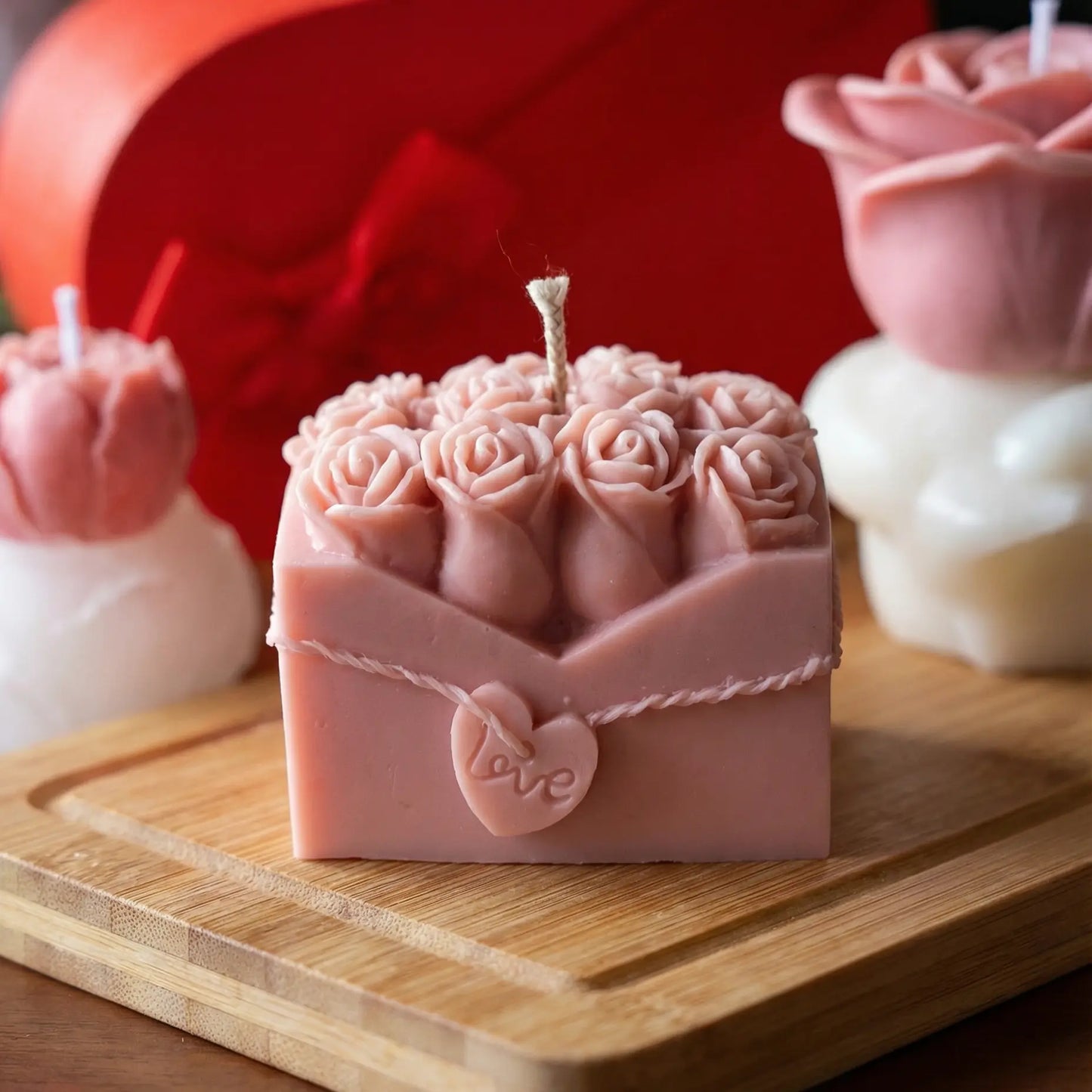 Pink rose-patterned candle in a box shape with 'love' heart on a wooden surface