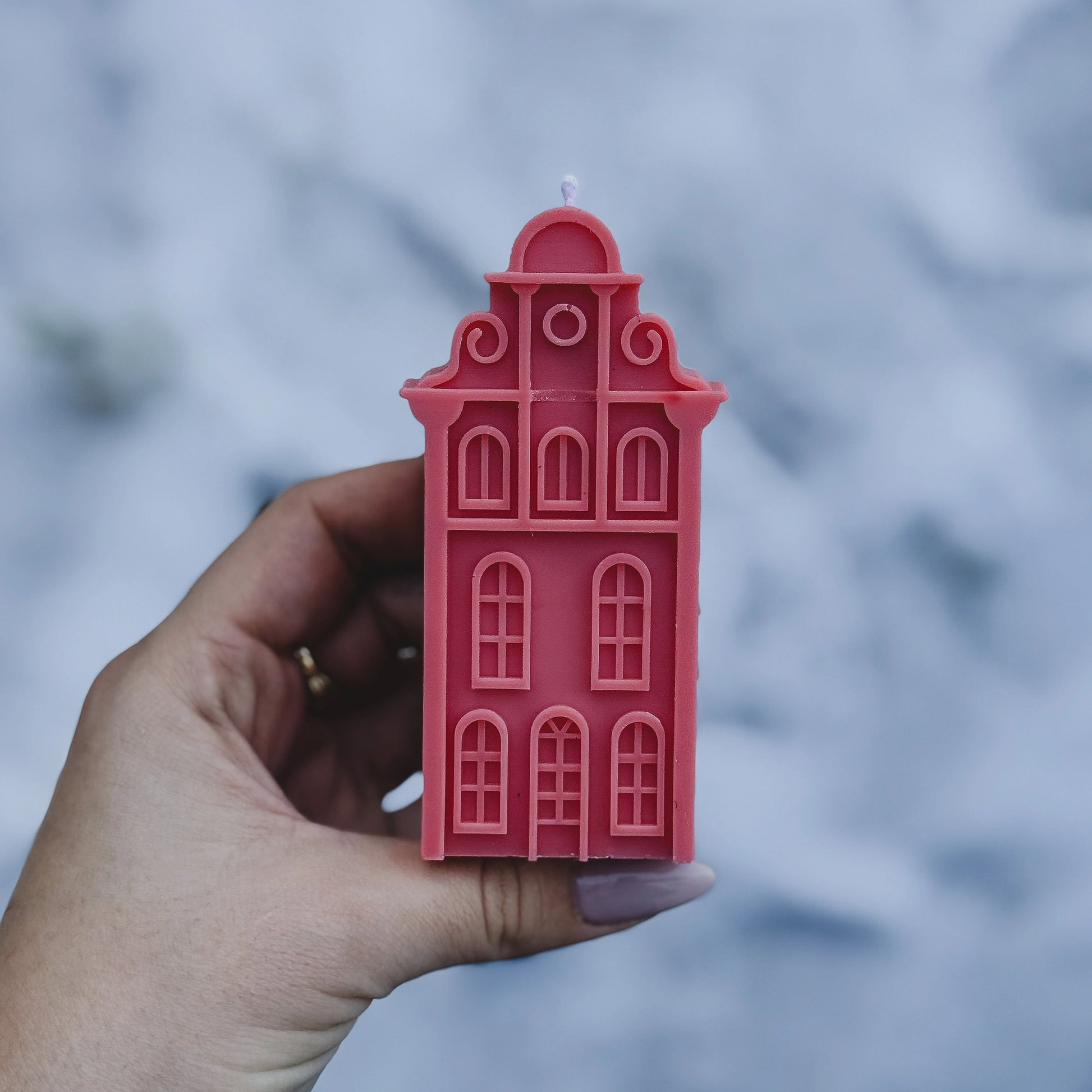 Pink Amsterdam house-shaped candle held by a hand on a textured surface.