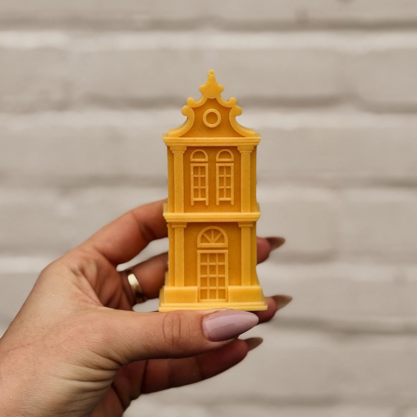 Hand holding a yellow Amsterdam canal house-shaped candle against a neutral background