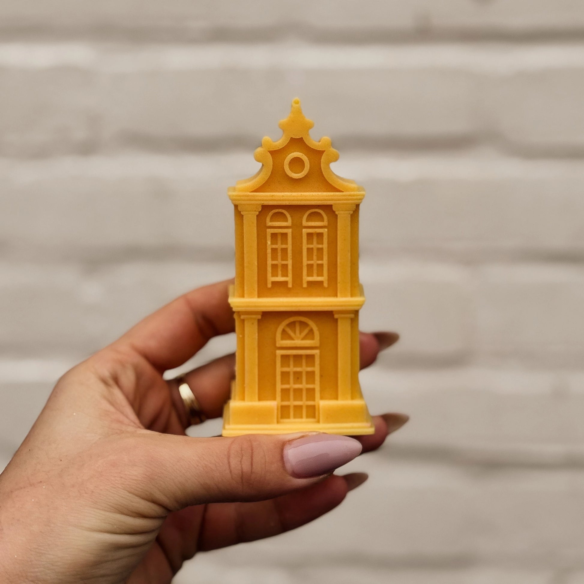 Hand holding a yellow Amsterdam canal house-shaped candle against a neutral background