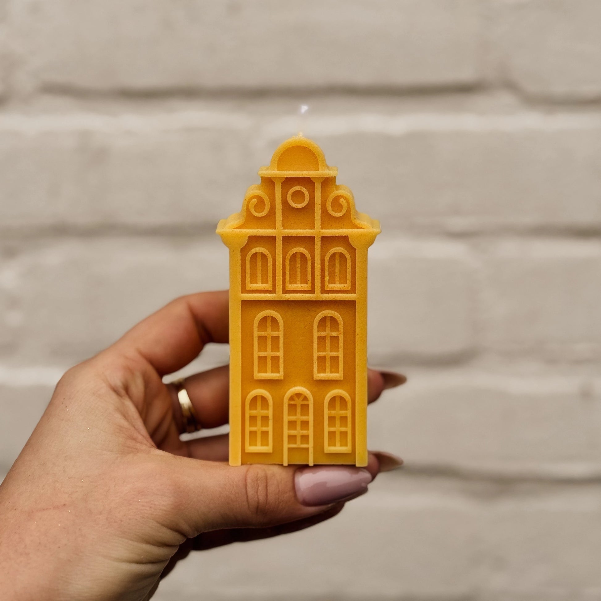 Hand holding a yellow Amsterdam canal house-shaped candle against a neutral background