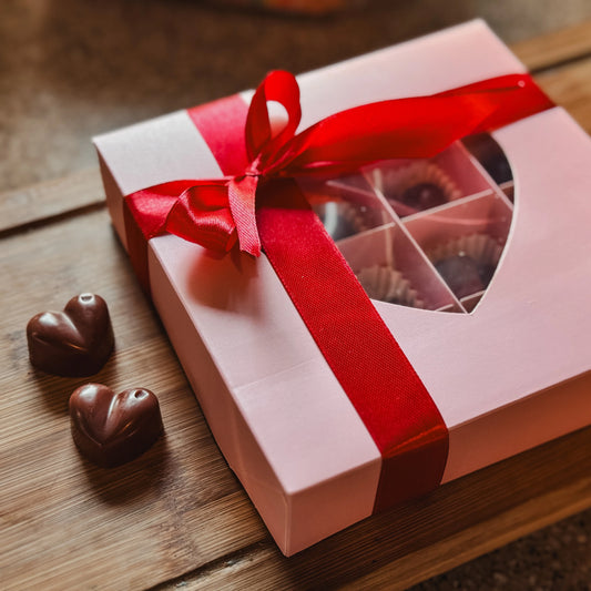 Pink gift box with red ribbon containing chocolate-shaped coffee-scented wax melts on a wooden surface