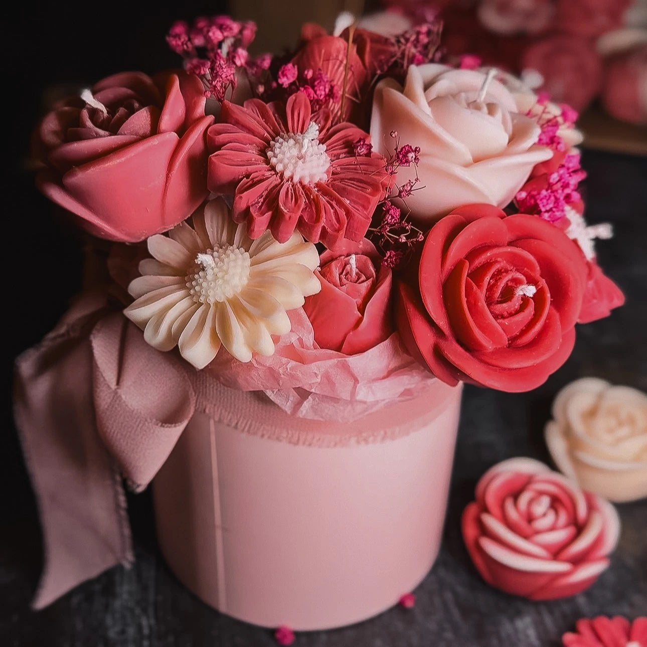 Pink, white and red flower-shaped candles in a bouquet box with a bow on a dark background