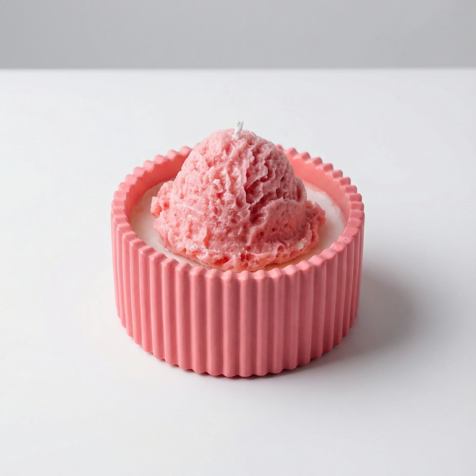 Pink ice cream candle with a textured candle container and a wick on a white background