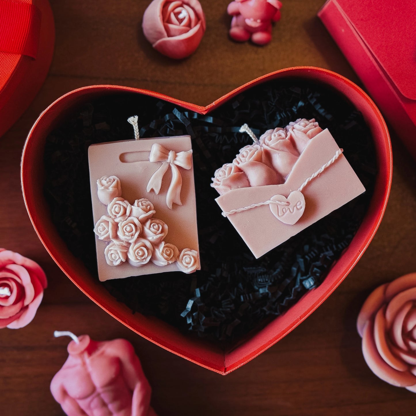 Heart-shaped box with decorative candles with floral and bow details on a wooden surface